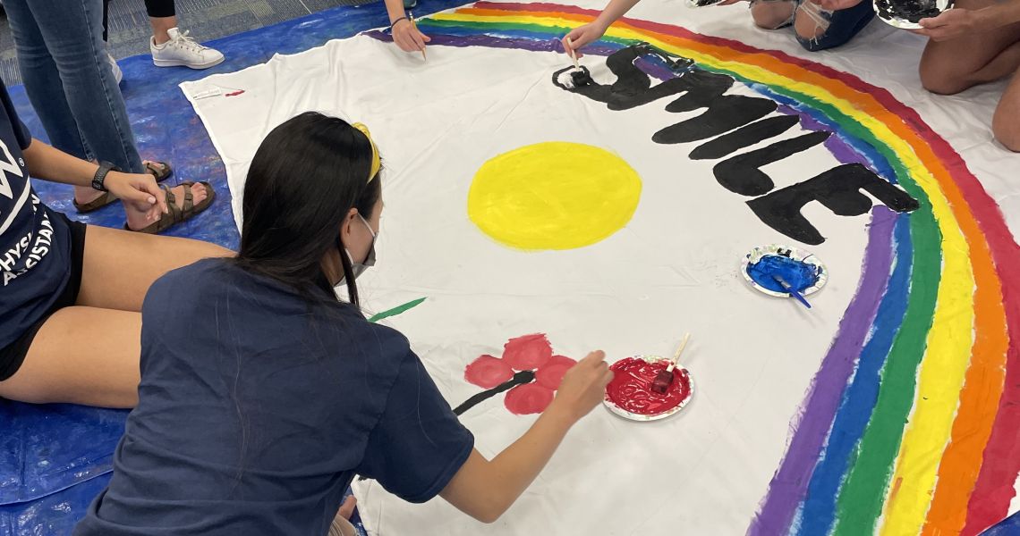 PA students painting a banner that has a rainbow and says 'Smile'